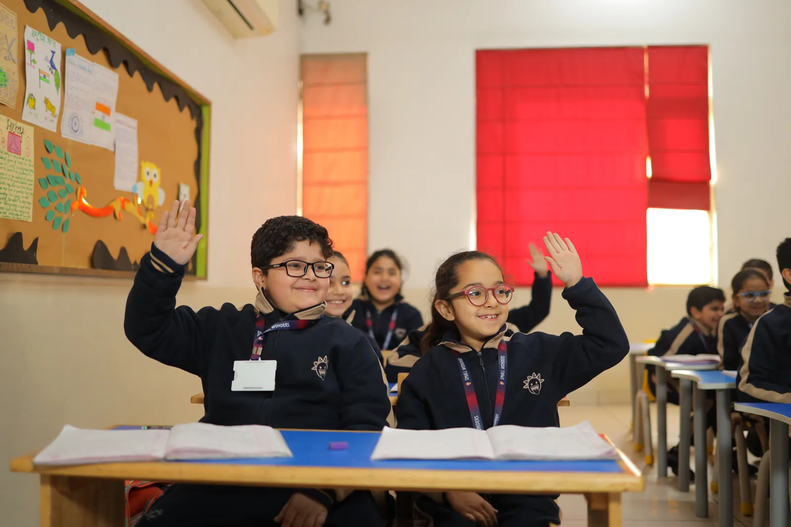 Learners with their hands up during a lesson in a bright classroom.