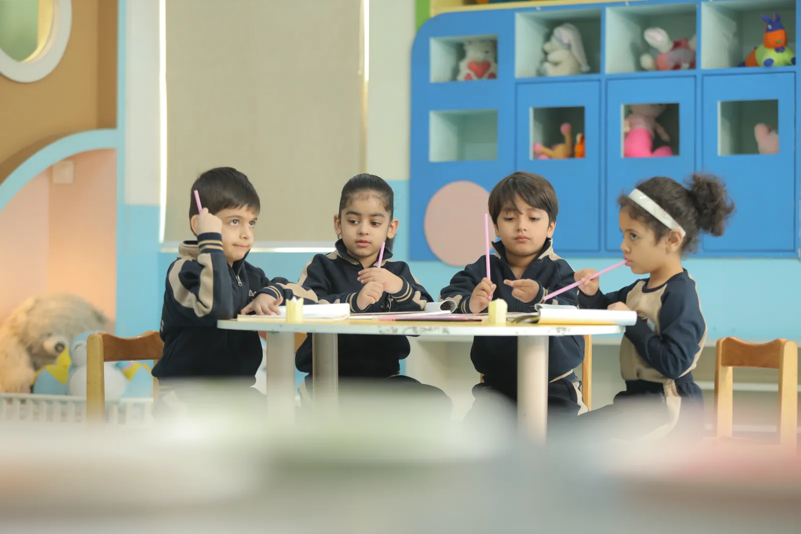 Young learners seated around a table in a colourful classroom.
