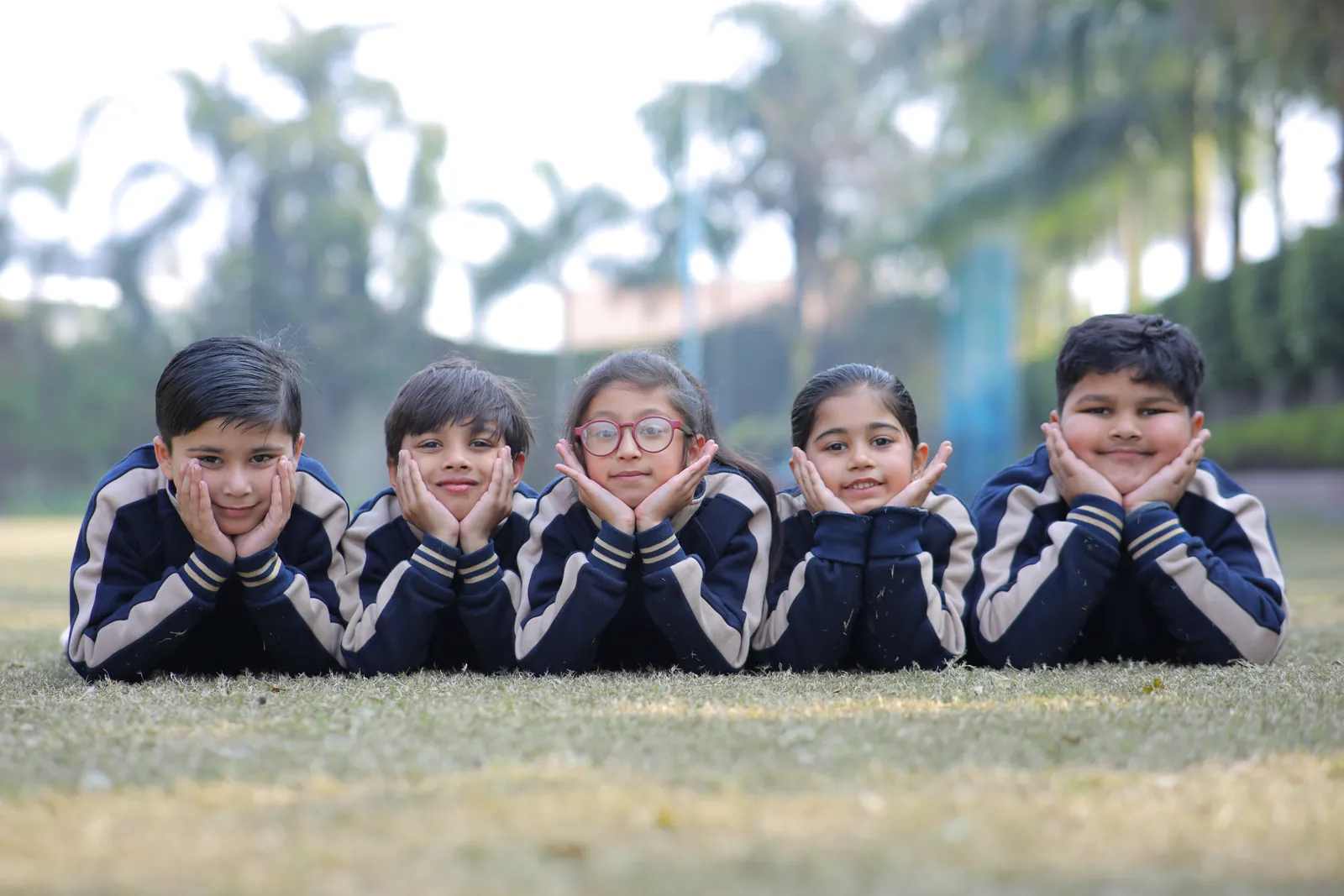 Five learners lying on the grass, chins in their hands, smiling at the camera.