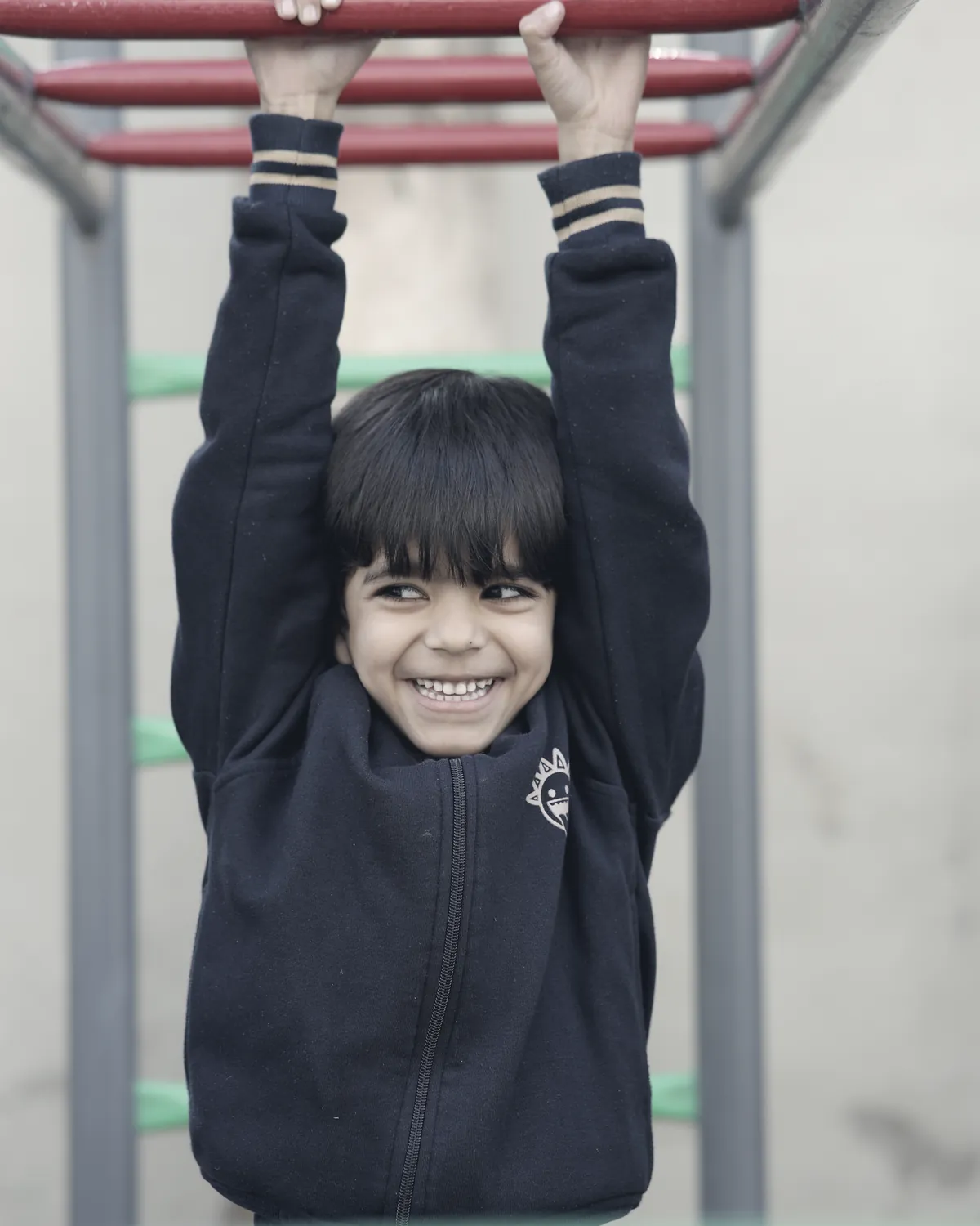 A learner hanging from the climbing frame in the play area, grinning.