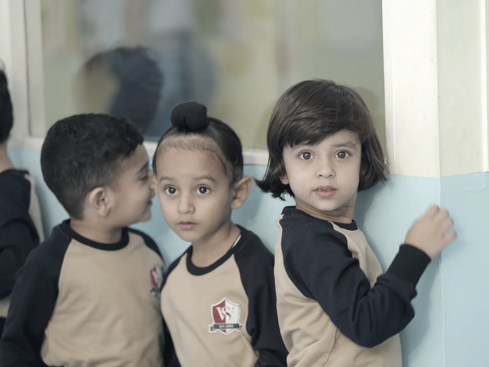 Three learners at the window of a Small Wonders classroom, one turning to look back.